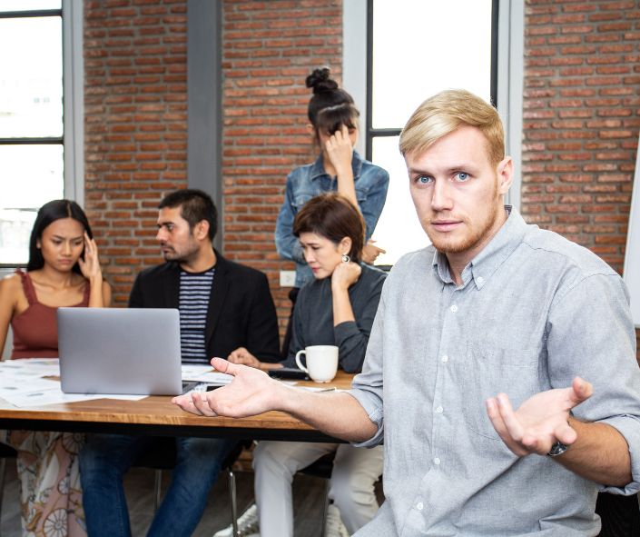 man looking confused with his team behind him at workplace