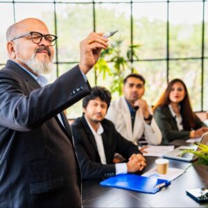 Smart Suit Wearing Office Director Holding A Pen and Presenting To Group of Younger Colleagues